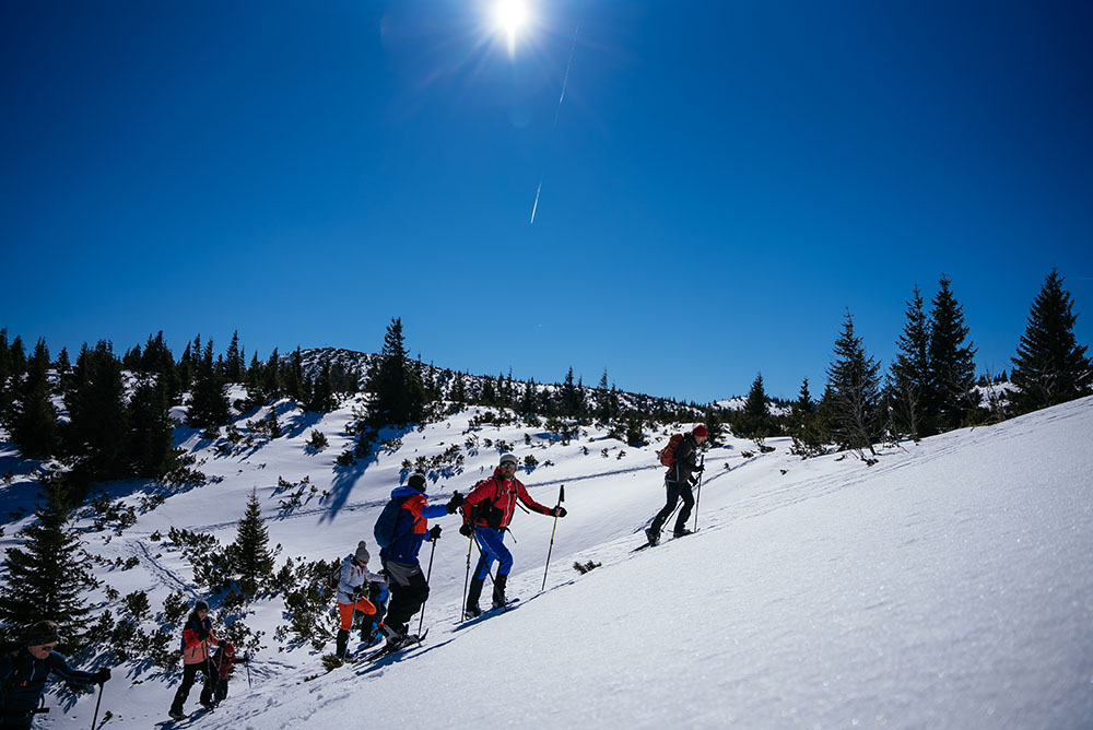 Gruppe Schneeschuhwanderer geht bergauf bei bestem Wetter Rax